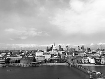 Bridge over river by buildings in city against sky