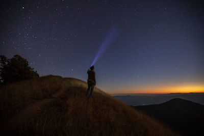 Tourist with illuminated flashlight standing on mountain against star field at night