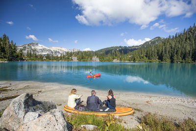 Family relaxing together at remote lake, brother paddling on lake.