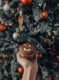 Cropped hand holding muffin by christmas tree