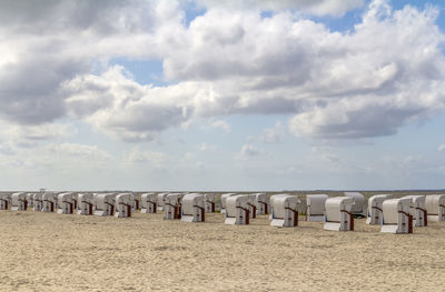 Hooded chairs on wooden posts at beach against sky