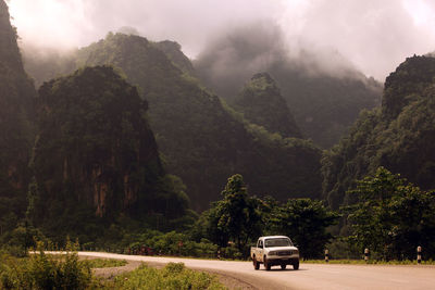 Car moving on road by mountains during foggy weather