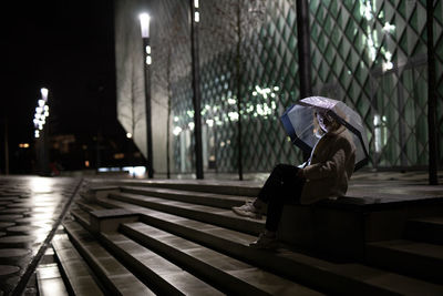 Woman with umbrella sitting on steps at night