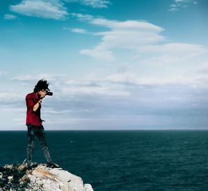 Photographer standing on rock over sea against sky