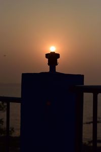 Illuminated lamp by sea against sky during sunset