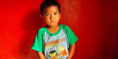 Portrait of boy standing against red wall