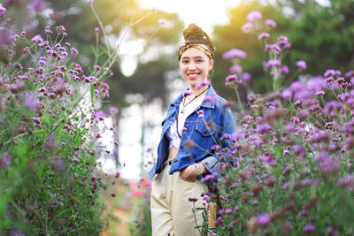 Portrait of young woman smiling while standing amidst purple flowers at park