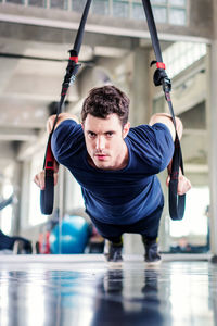 Sportsman doing exercise with fitness straps to strengthen his abdominal muscle in gym.
