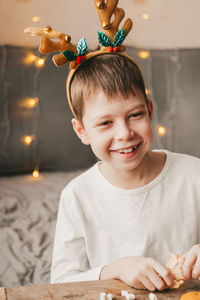 Portrait of a boy in reindeer christmas antlers on the background of an orange garland.