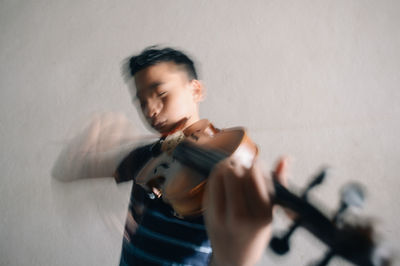 An asian boy playing violin against a wall