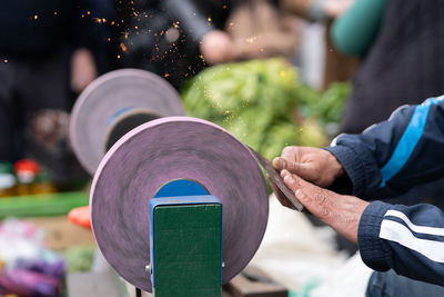 Master sharpens ax on electric sharpener with bright sparks and holds blade with his brutish fingers