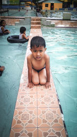 Portrait of shirtless wet boy kneeling at poolside