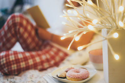 Midsection of woman reading book while having donuts by illuminated decoration at home