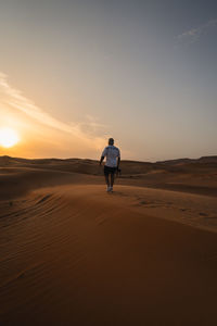 Rear view of man standing at beach against sky during sunset