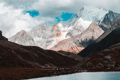 Crowd of people standing by lake against mountain range