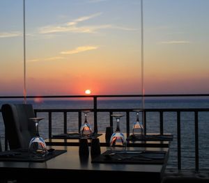 People sitting on table by sea against sky during sunset