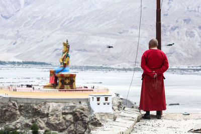 Rear view of monk standing at temple against mountains