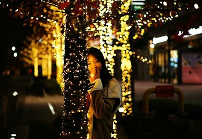 Young woman with christmas tree in city at night