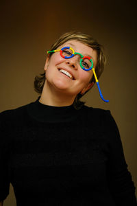 Portrait of smiling woman wearing novelty glasses against colored background