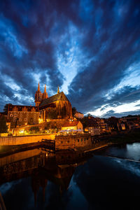 Illuminated building by river against sky at dusk