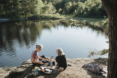 Two senior women preparing hot meal at campsite at lakeshore