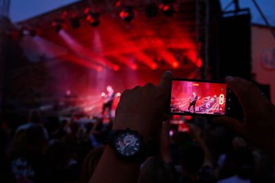 Person standing in front of stage, recording live music concert on smartphone