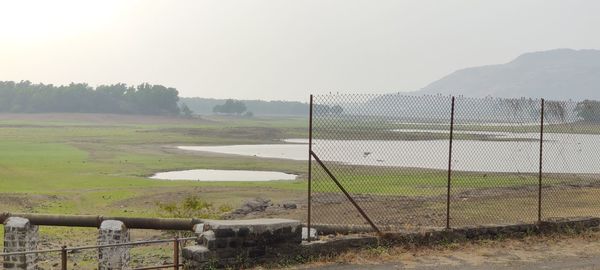 Scenic view of field seen through fence against sky