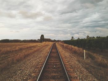 Railroad tracks on agricultural field against sky