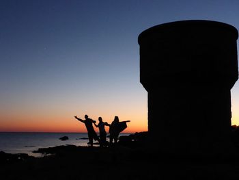 Silhouette people on rocks at sunset