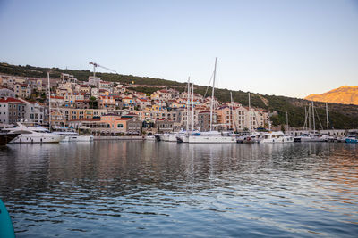 Sailboats moored in harbor by city against clear sky