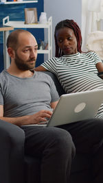 Husband using laptop while sitting with pregnant wife