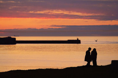 Silhouette couple against orange sky during sunset