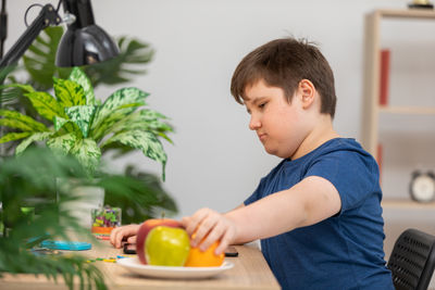 Side view of boy holding apple while sitting at home