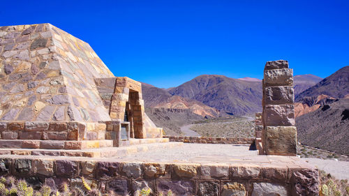 Built structure against blue sky with mountain range in background