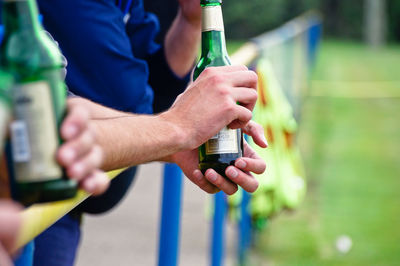 Midsection of men holding beer bottle while standing by railing