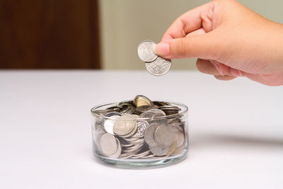 Cropped hand putting coins in container on table