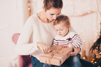 Smiling mother and daughter holding gift box at home