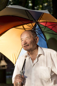 A pensioner under a multi-colored umbrella smiles in the sun.