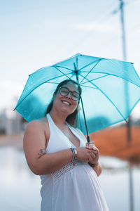 Young woman with umbrella standing against sky