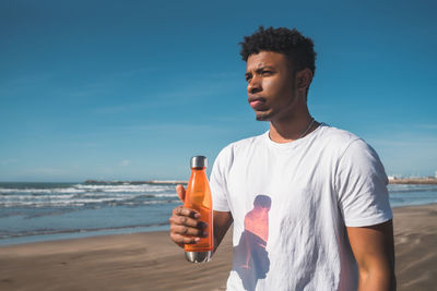 Young man standing at beach against sky