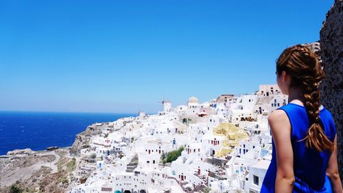 Rear view of woman standing by sea against clear blue sky