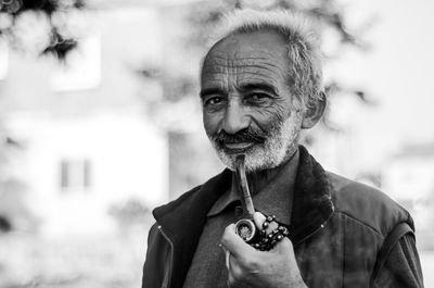 Portrait of senior man holding smoking pipe while standing outdoors
