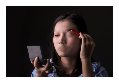 Close-up of woman applying make-up against black background