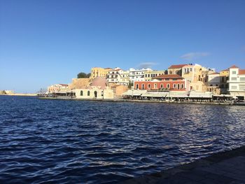 Buildings by sea against clear blue sky
