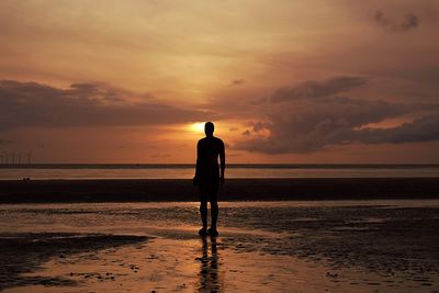 Silhouette man standing on sand against sea during sunset