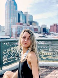 Thoughtful young woman sitting against modern buildings in city