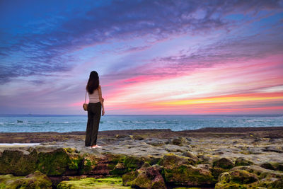 Man standing on rock by sea against sky during sunset