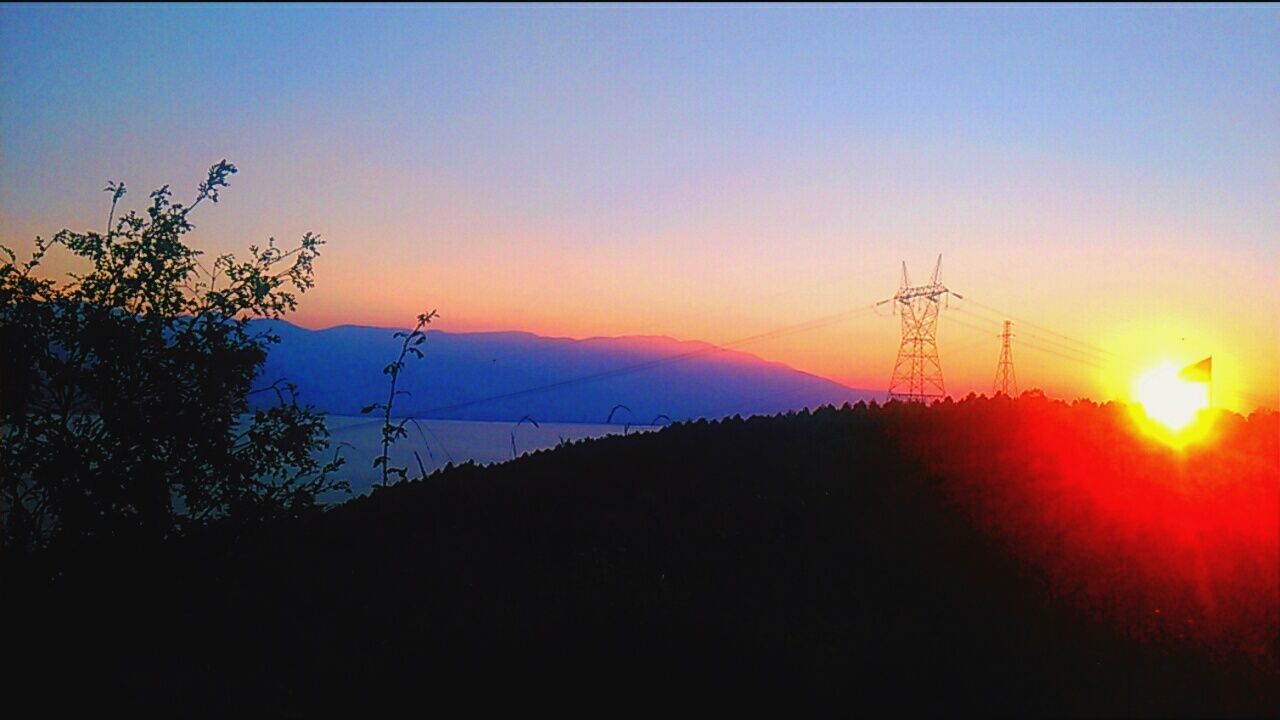silhouette, sunset, scenics, tranquil scene, mountain, tranquility, beauty in nature, sun, nature, copy space, landscape, clear sky, idyllic, electricity pylon, dark, calm, outdoors, sky, power line, remote, outline, mountain range, no people, non-urban scene, electricity tower