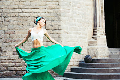 Beautiful woman holding skirt while standing on street against building