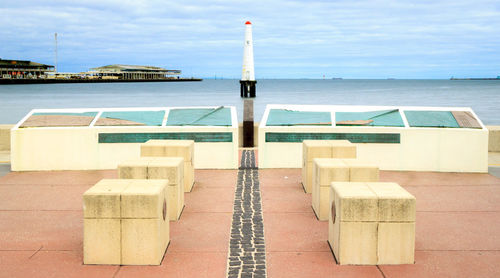 Stone chairs against sea and lighthouse against sky at port melbourne